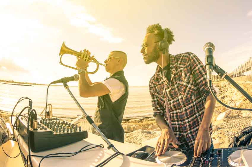 Trendy hipster dj playing summer hits at sunset beach party with