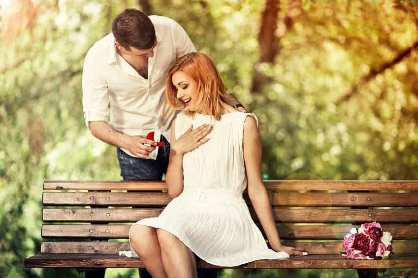 Man holding red box with ring making propose to his girlfriend outdoors.