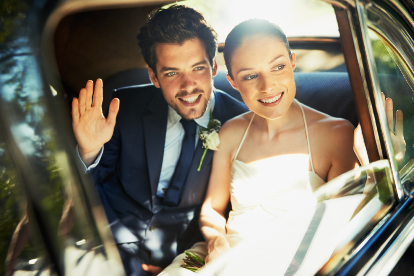 Shot of a newlywed couple looking out the window of a car and waving