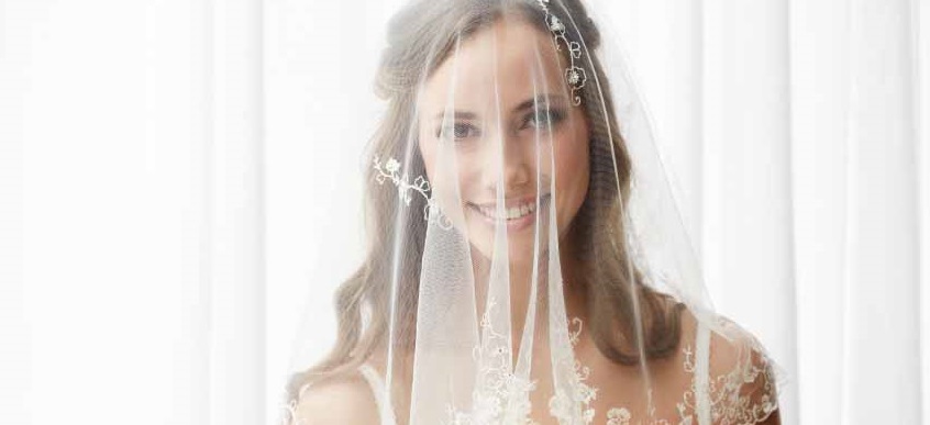 Excited young bride in veil holding bouquet, portrait