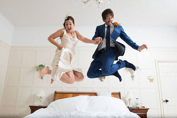 bride and groom jumping on a bed
