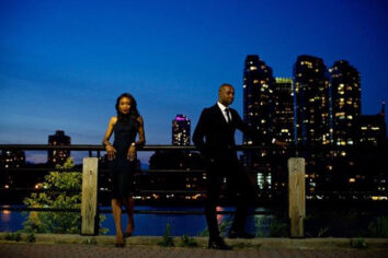 an engaged couple is posing against a city skyline at dusk