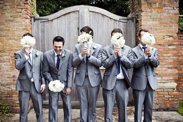 groomsmen taking photograph holding wedding bouquets