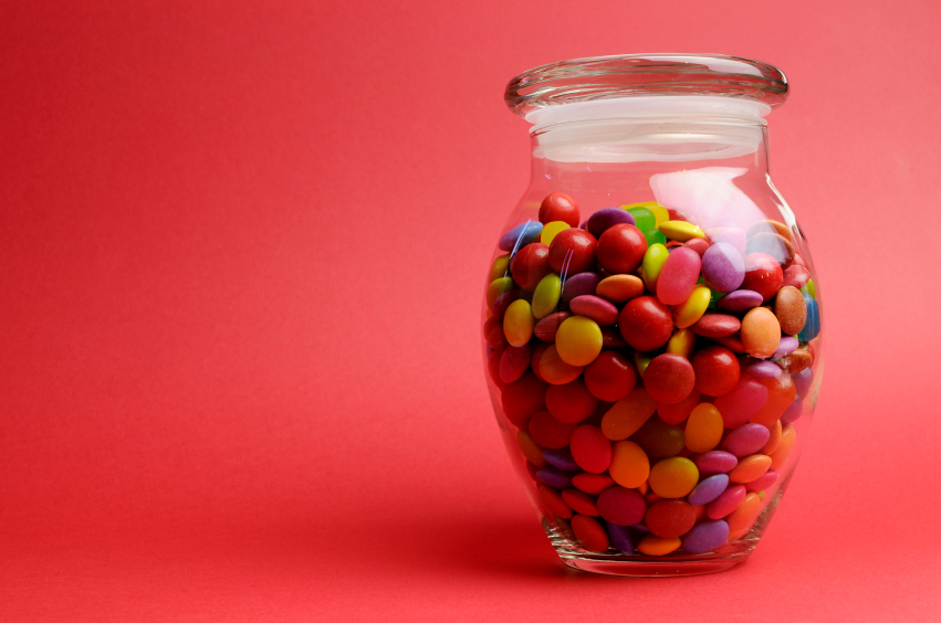 Glass Jar full of bright colorful lollies and candy with closed lid against a red orange background with copy space for your text here.