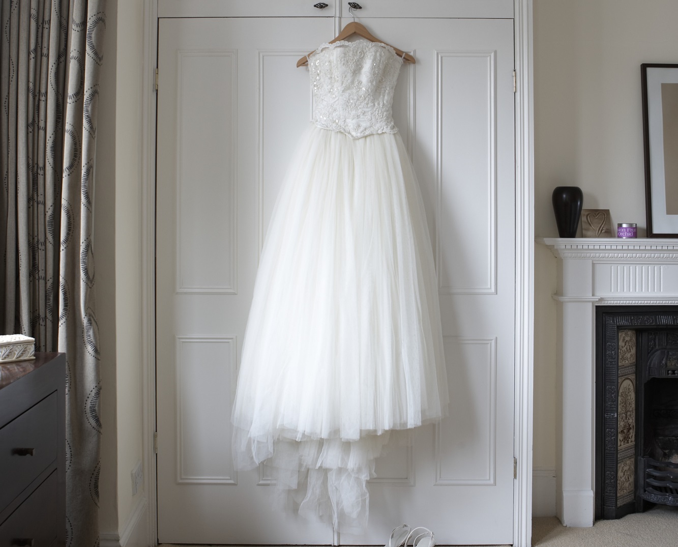 Wedding dress hanging on wardrobe doors, white shoes on floor