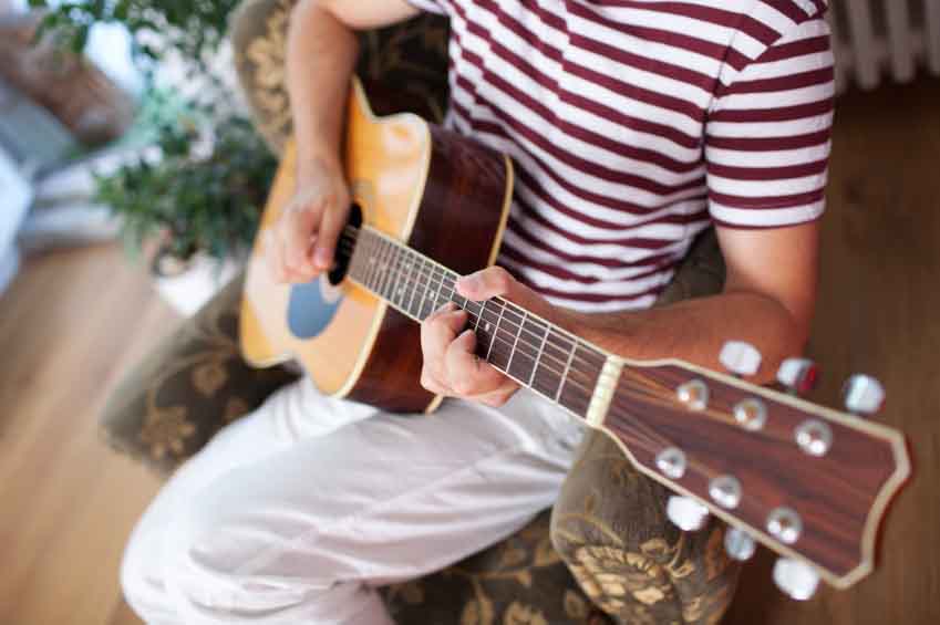 Young man sitting in armchair, playing a guitar