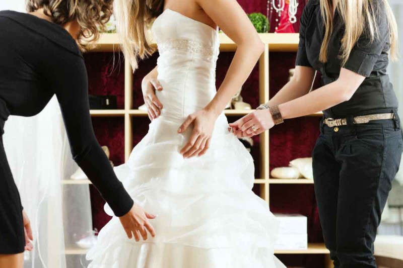 Lady trying on wedding dress with bridesmaids