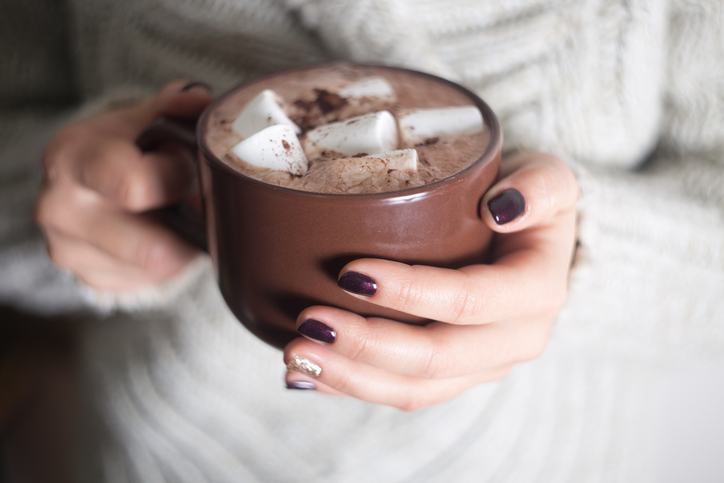 Brown cup with cocoa and marshmallow in the hands of the girl. Manicure gel nail.