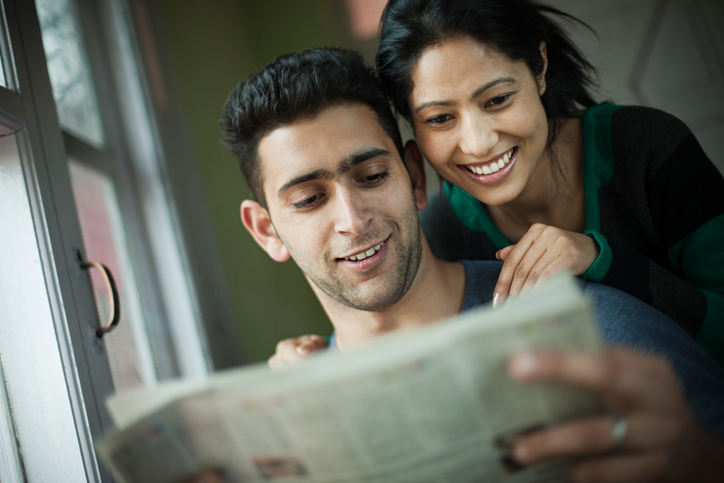 Happy romantic couple reading newspaper together.