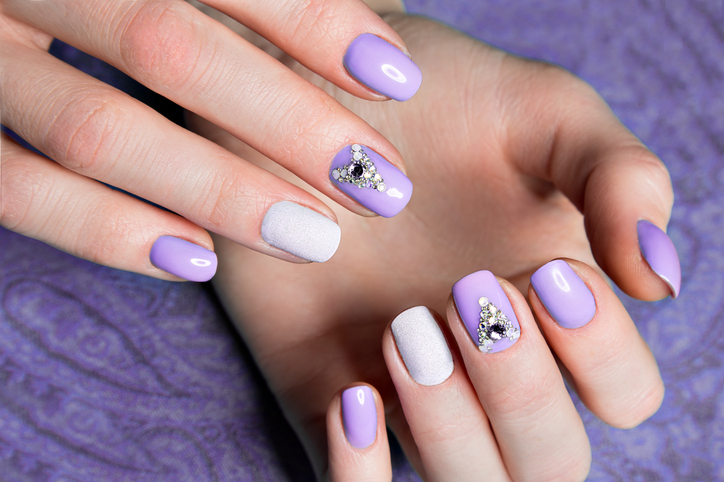 Beautiful purple manicure with crystals on female hand. Close-up.