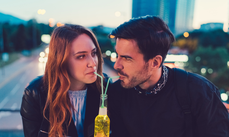 Smiling couple at the bridge drinking cider from one bottle with drinking straw