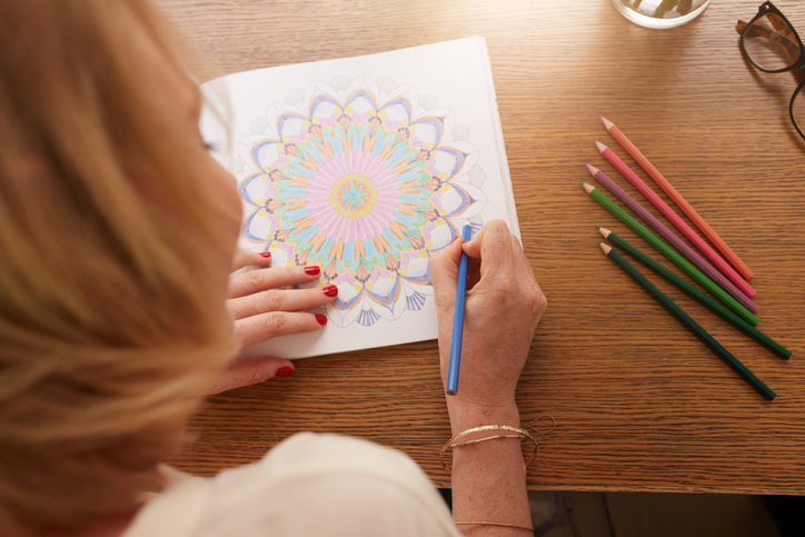 Overhead view of woman drawing in adult coloring book with color pencils. Anti stress exercise at home.