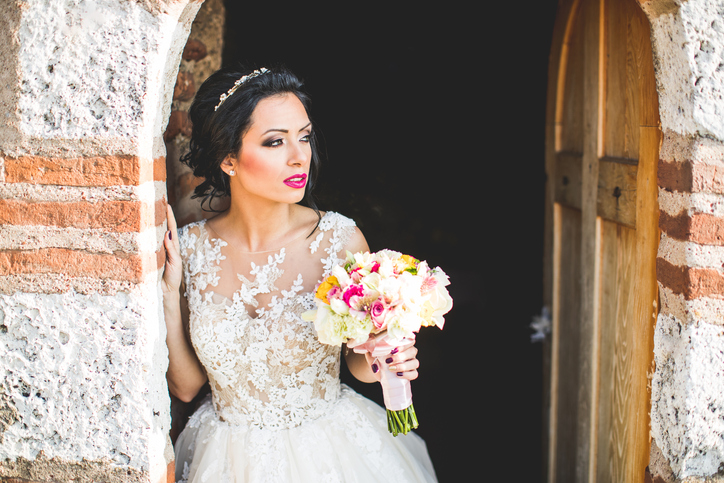 Bride leaning on the brick wall holding flowers and posing while looking away