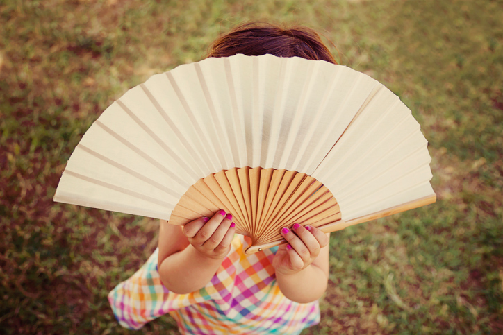 Little girl hiding behind a hand-held fan