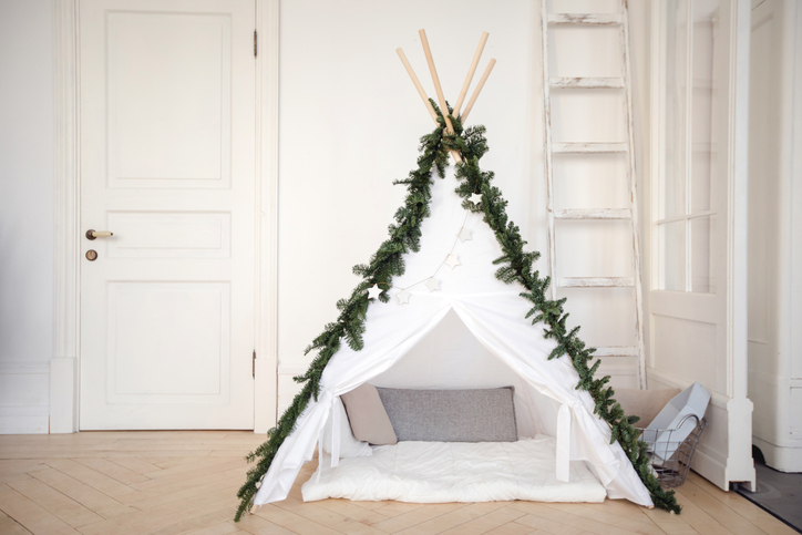 Beautiful comfortable tent with pillows inside created at home and decorated with pine branches.