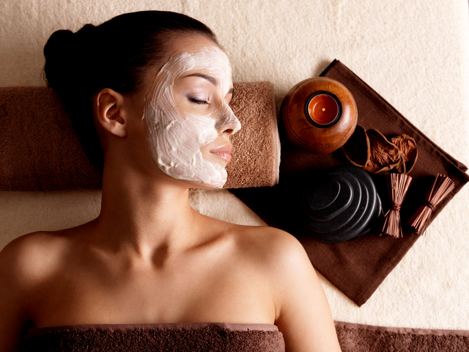 Young woman relaxing with facial mask on face at beauty salon- indoors