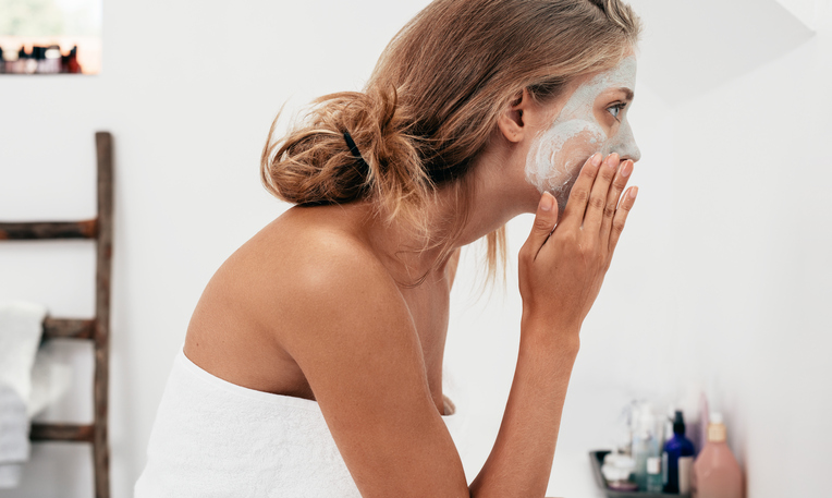 Side view shot of young woman applying facial cosmetic mask in bathroom.  Female taking care of her face skin.