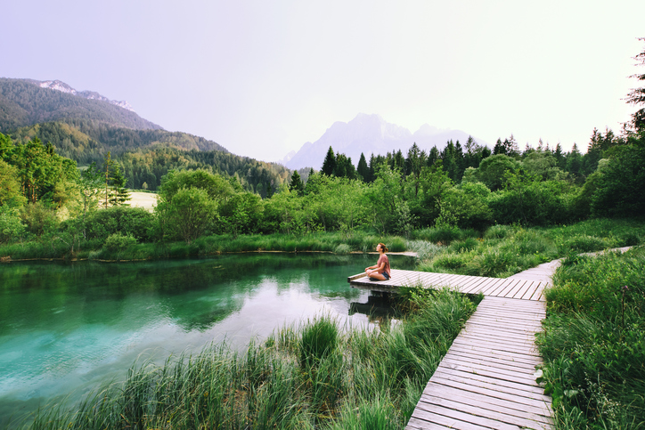 Young woman doing yoga and meditating in lotus position on the background of nature. Concept of Meditation, Relaxation and Healthy Life. Slovenia, Europe.