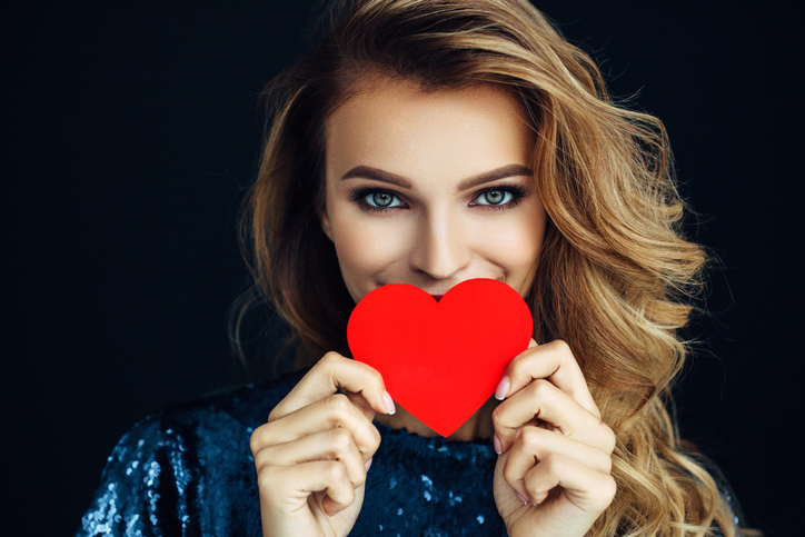 Studio shot of young beautiful woman holding artificial heart. Professional make-up.