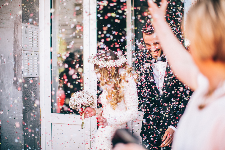 Photo of just married couple. Guests are throwing confetti in the air.