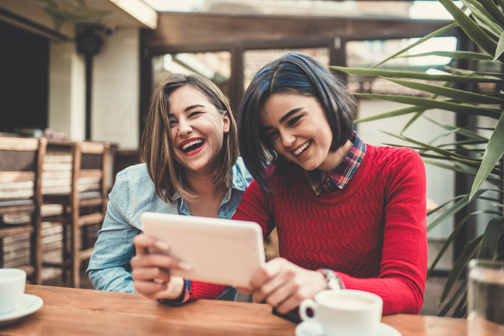 Two Female Frineds Holding Tablet and Laughing in Coffee Shop