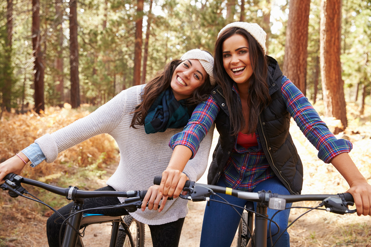 Lesbian couple on bikes in a forest look to camera