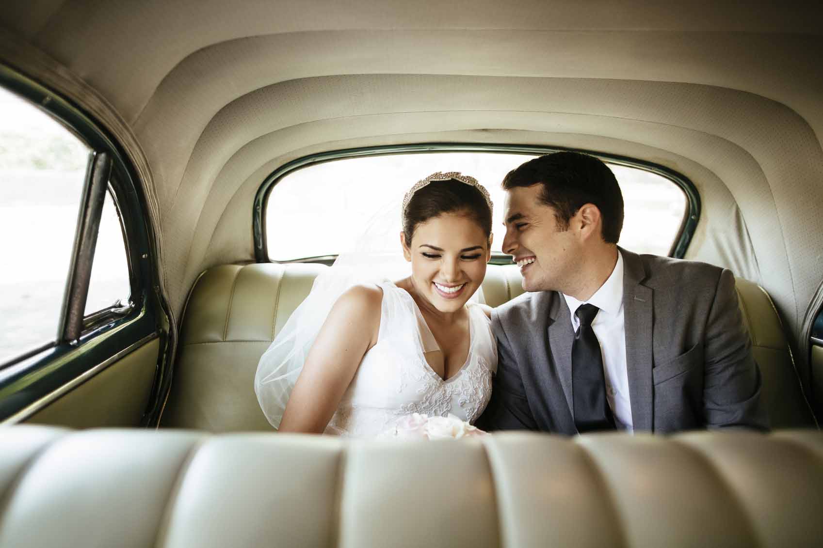 Beautiful Hispanic newlyweds laughing in backseat