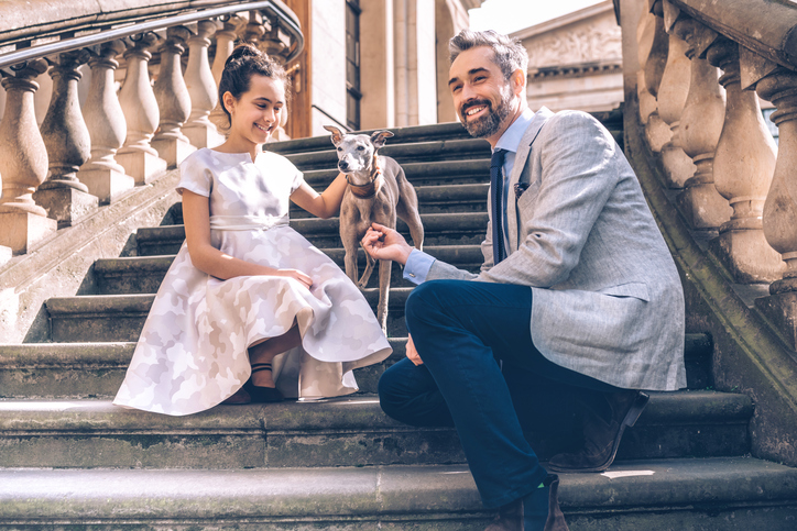 happy elegant father sitting on stairs with festive dressed teenage girl and dog
