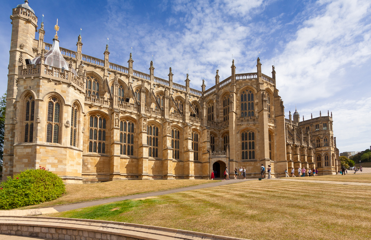 St George's Chapel, Windsor Castle, Berkshire, England. The original castle was built in the 11th century and is the longest-occupied palace in Europe. Landscaped, grass, tourists and vivid blue sky with clouds are in the image.