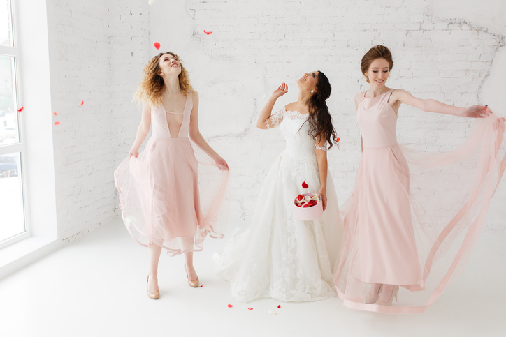 Bride and bridesmaids dancing in white loft studio with flying petals. Full-lenght portrait