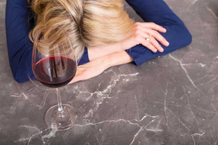 Depressed woman with wine glass resting her head on kitchen counter