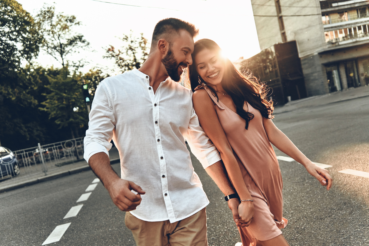 Beautiful young couple holding hands and smiling while walking through the city street