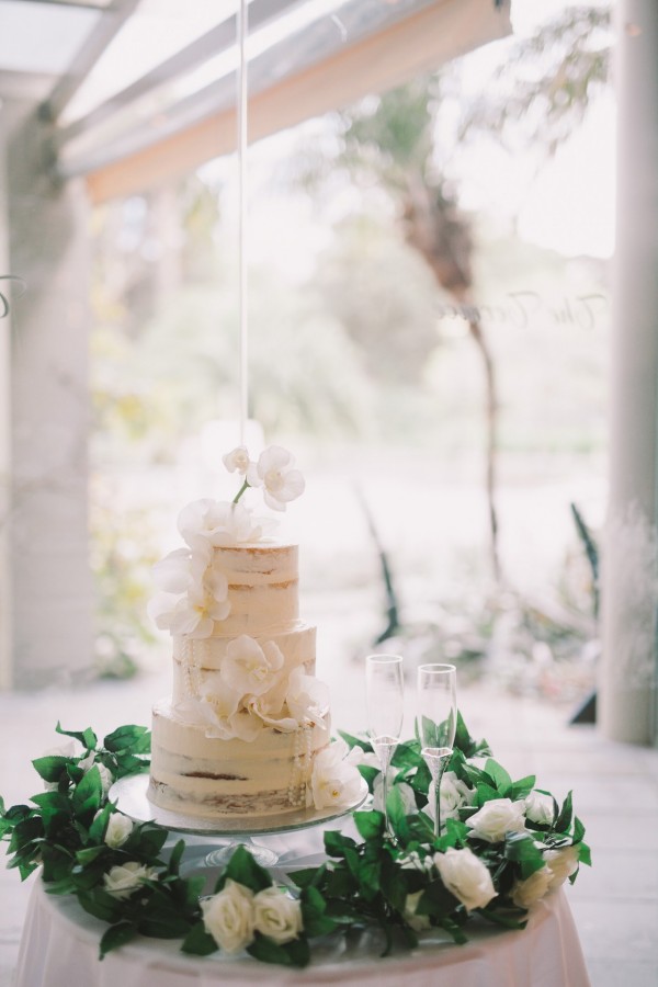 White semi naked wedding cake with orchids and pearls draped over it