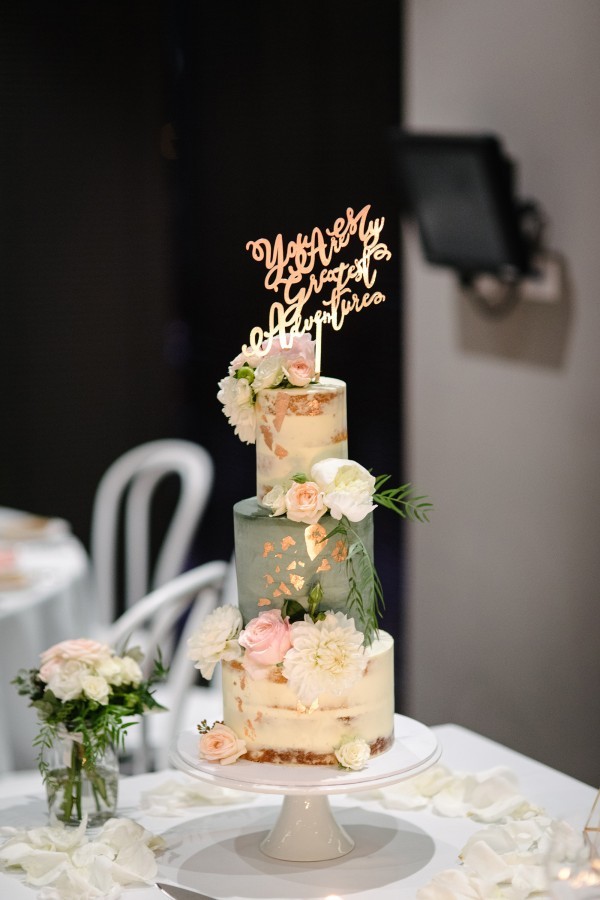 Gorgeous wedding cake comprised of three tiers, with flowers, greenery and laser cut quote cake topper