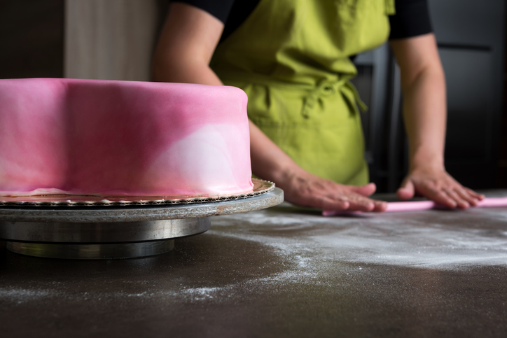 Woman preparing pink fondant for cake decorating, focus on cake