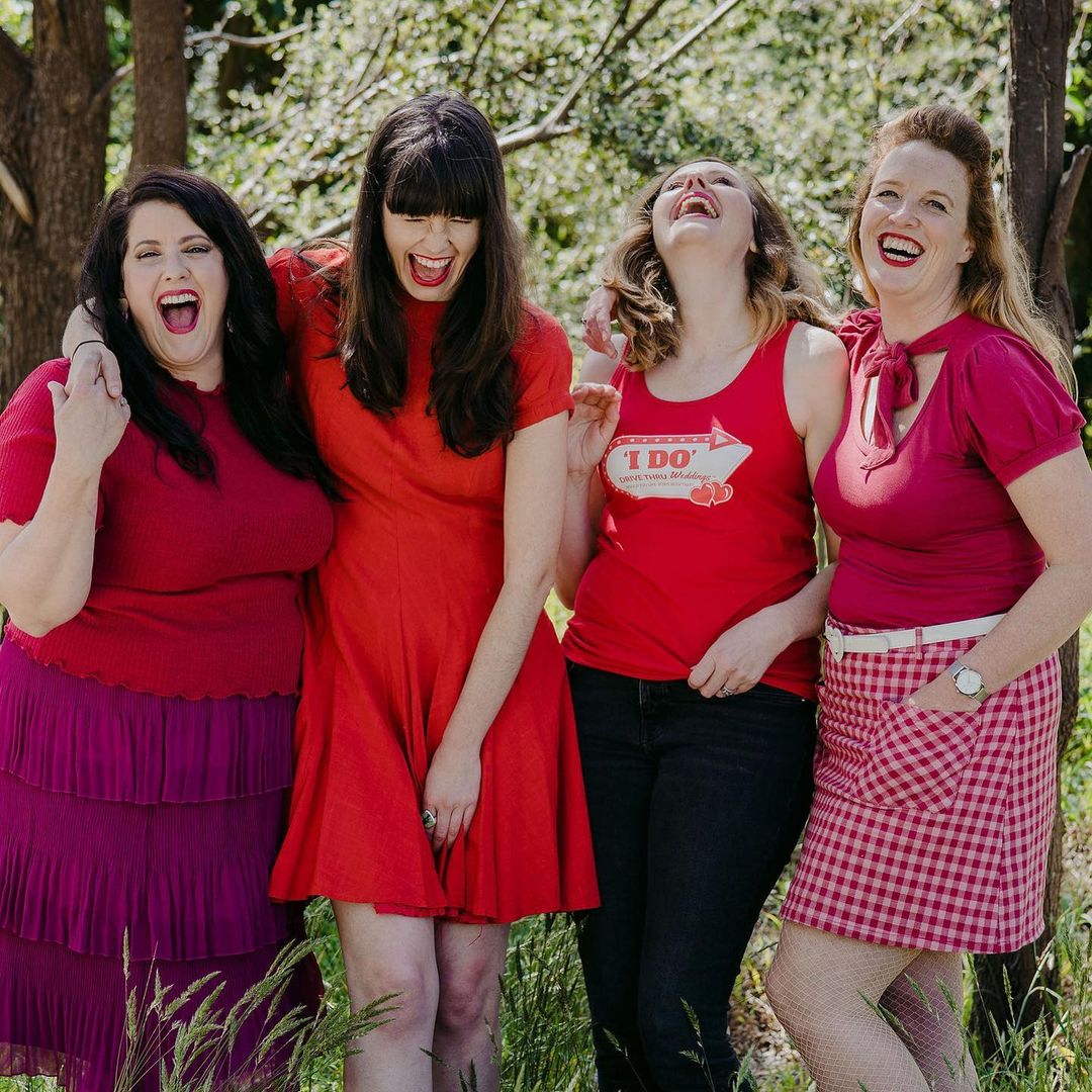 four female celebrants wearing red anf pink and smilings and laughing. the founders of I DO DRIVE THRU