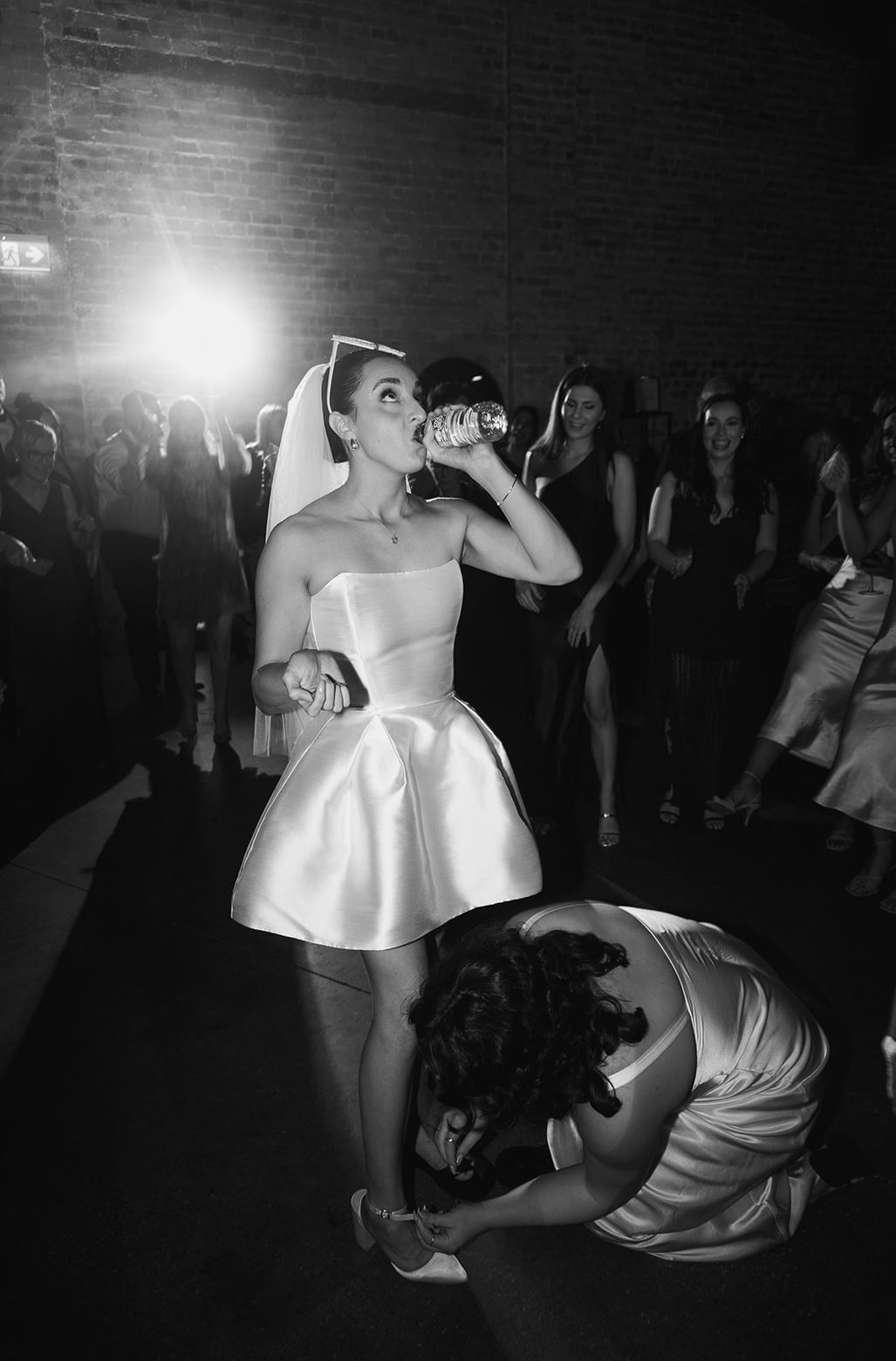 black and white image of bride getting her shoe fixed