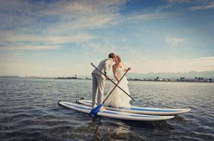 bride and groom kissing while on surfing board